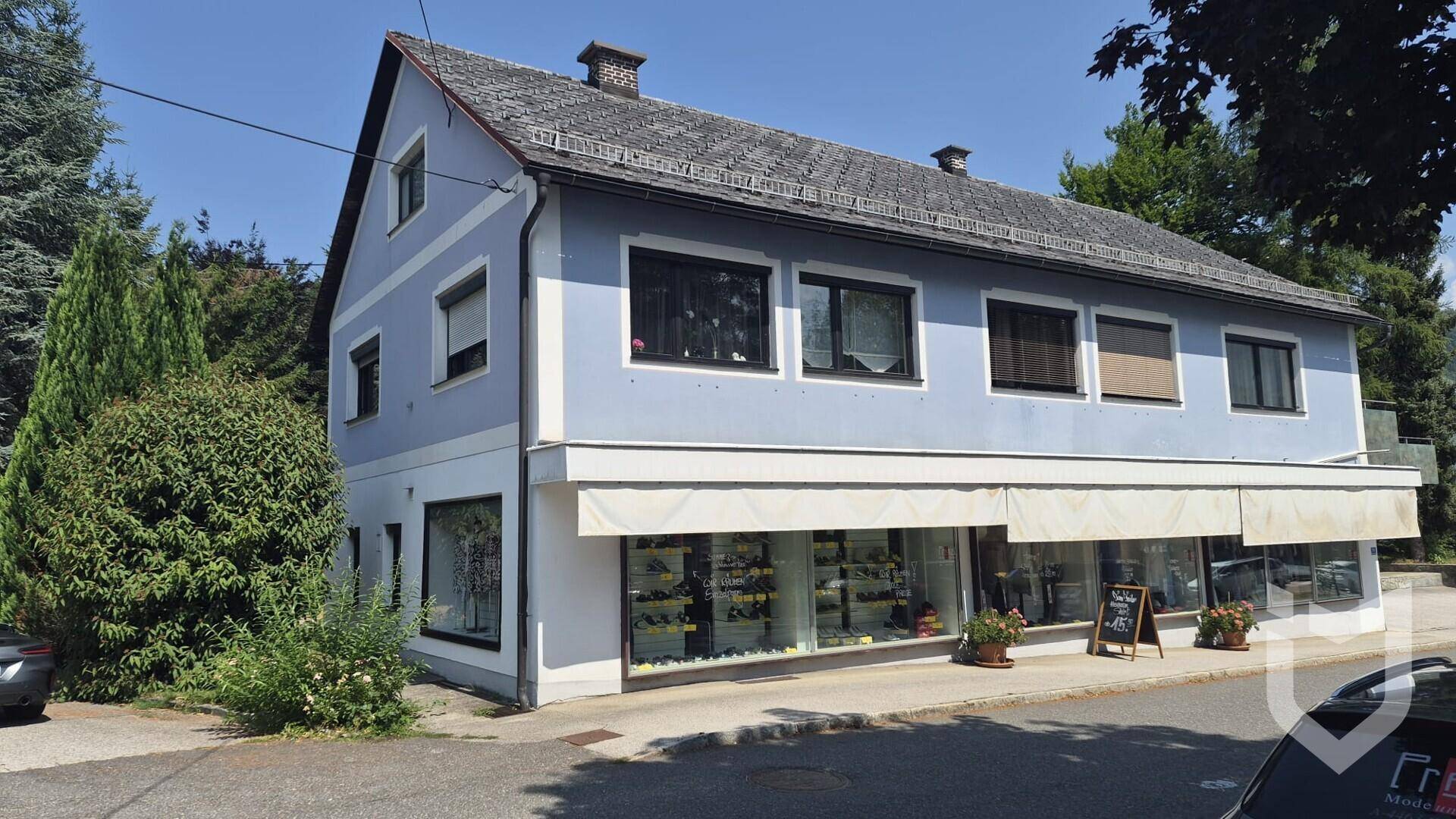 Gesamtansicht des Gewerbegebäudes mit Schaufenstern, Dach und umliegender Vegetation.
