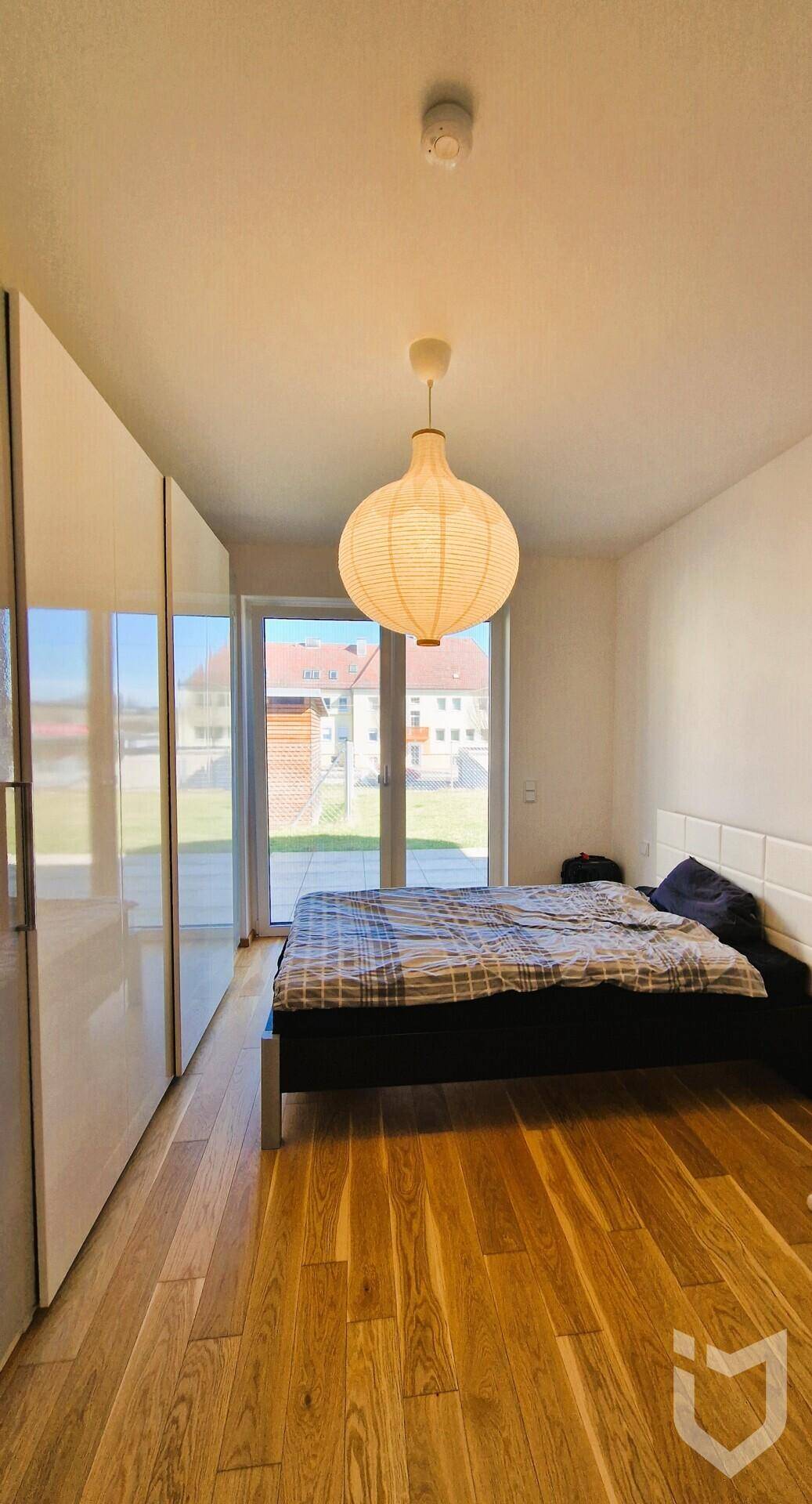 Helles Schlafzimmer mit Holzboden, Einbauschränken und Zugang zum Außenbereich.