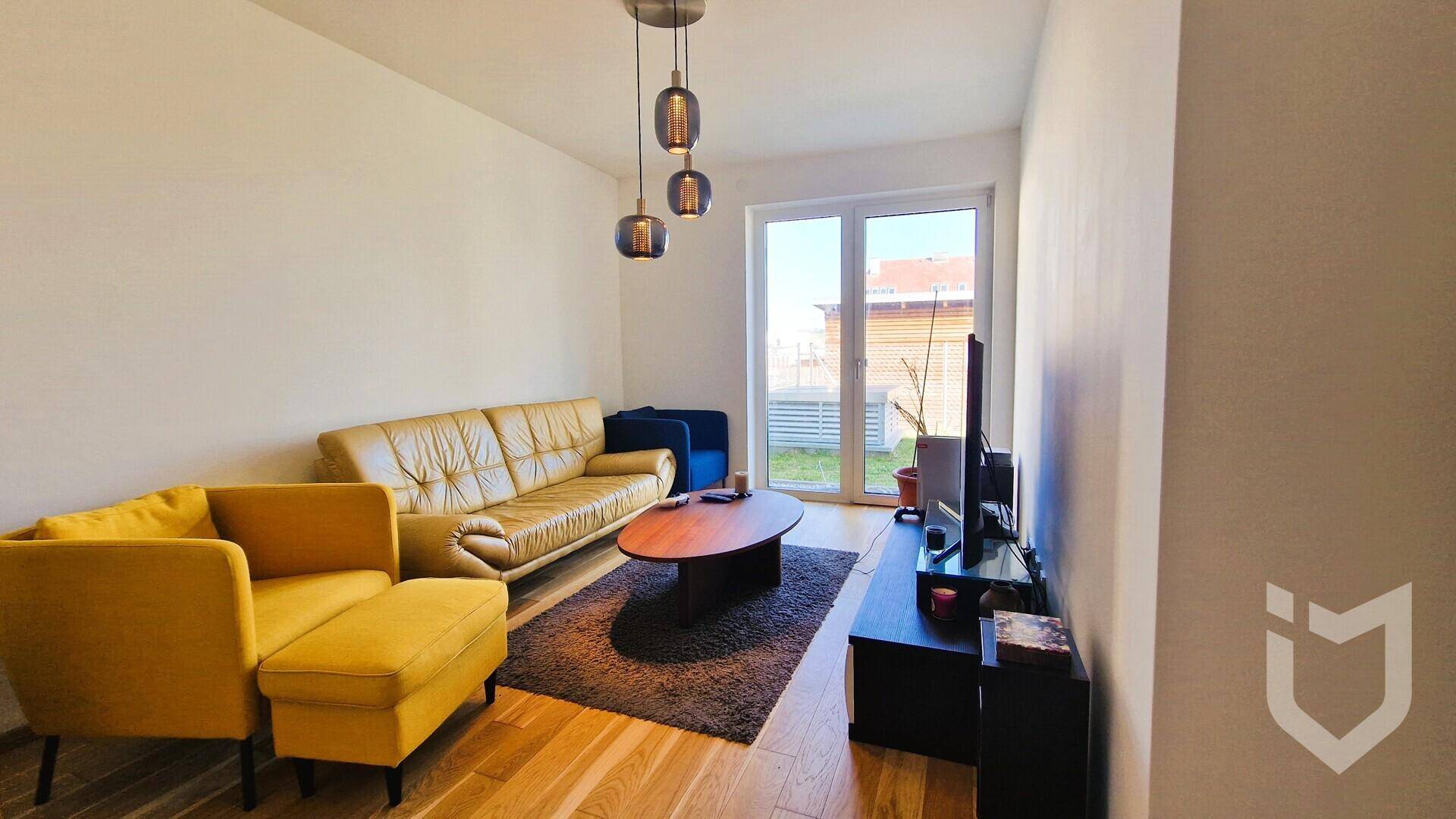 Gemütliches Wohnzimmer mit Sofa, Fernseher und Zugang zu einem kleinen Balkon.
