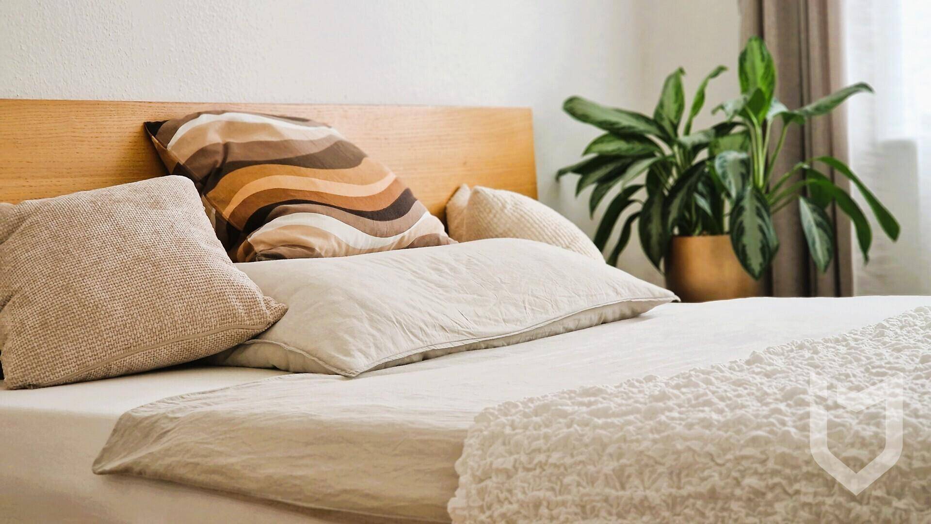 Nahaufnahme des Bettes mit beigen Kissen und einer weißen Tagesdecke im Schlafzimmer.