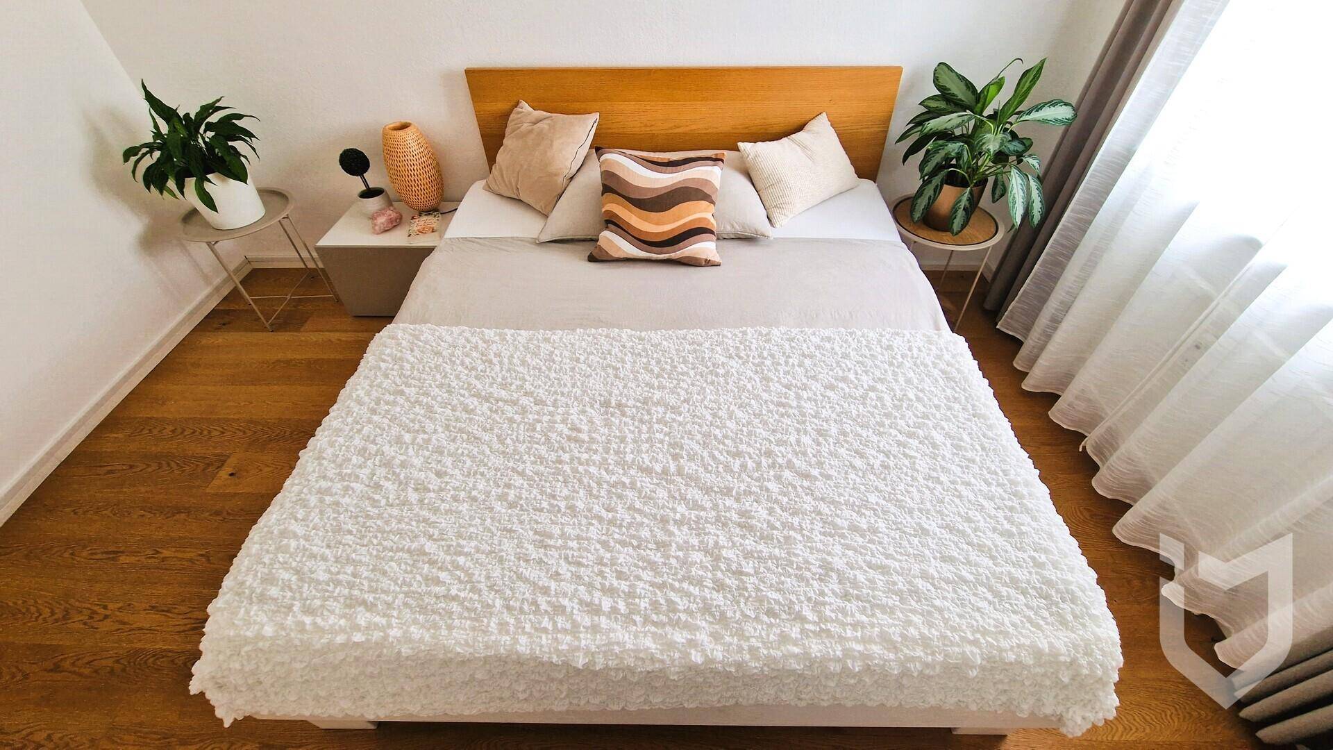 Blick von oben auf das ordentlich gemachte Bett mit weißer Decke im Schlafzimmer.