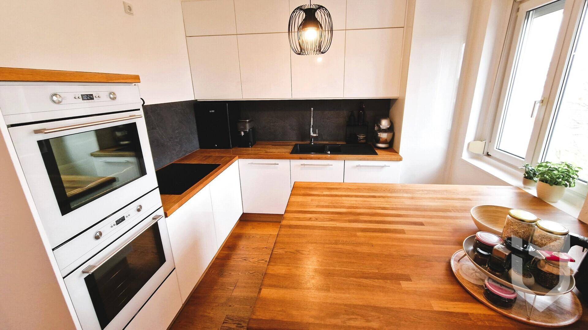 Moderne Küche mit weißen Schränken, Holzarbeitsplatten und integrierten Backöfen.