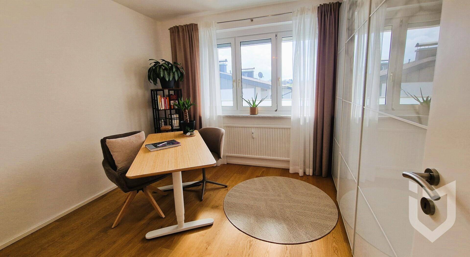 Arbeitszimmer mit Schreibtisch, Bürostühlen und einem Fenster mit Blick nach draußen.