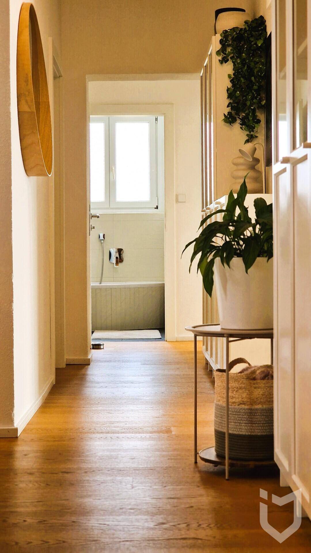 Heller Flur mit Holzboden, der zu einem Badezimmer mit Badewanne führt.