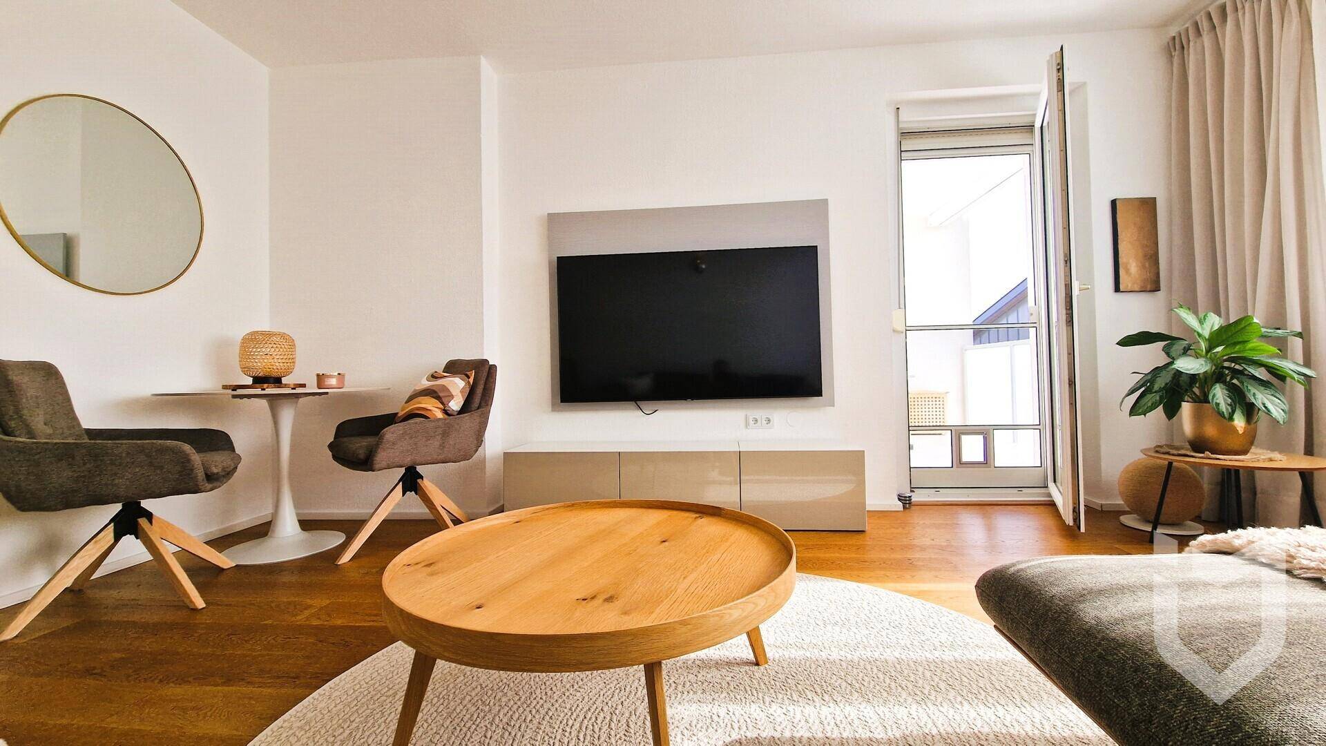 Wohnzimmer mit Holzboden, Wandfernseher und einem runden Spiegel als dekoratives Element.