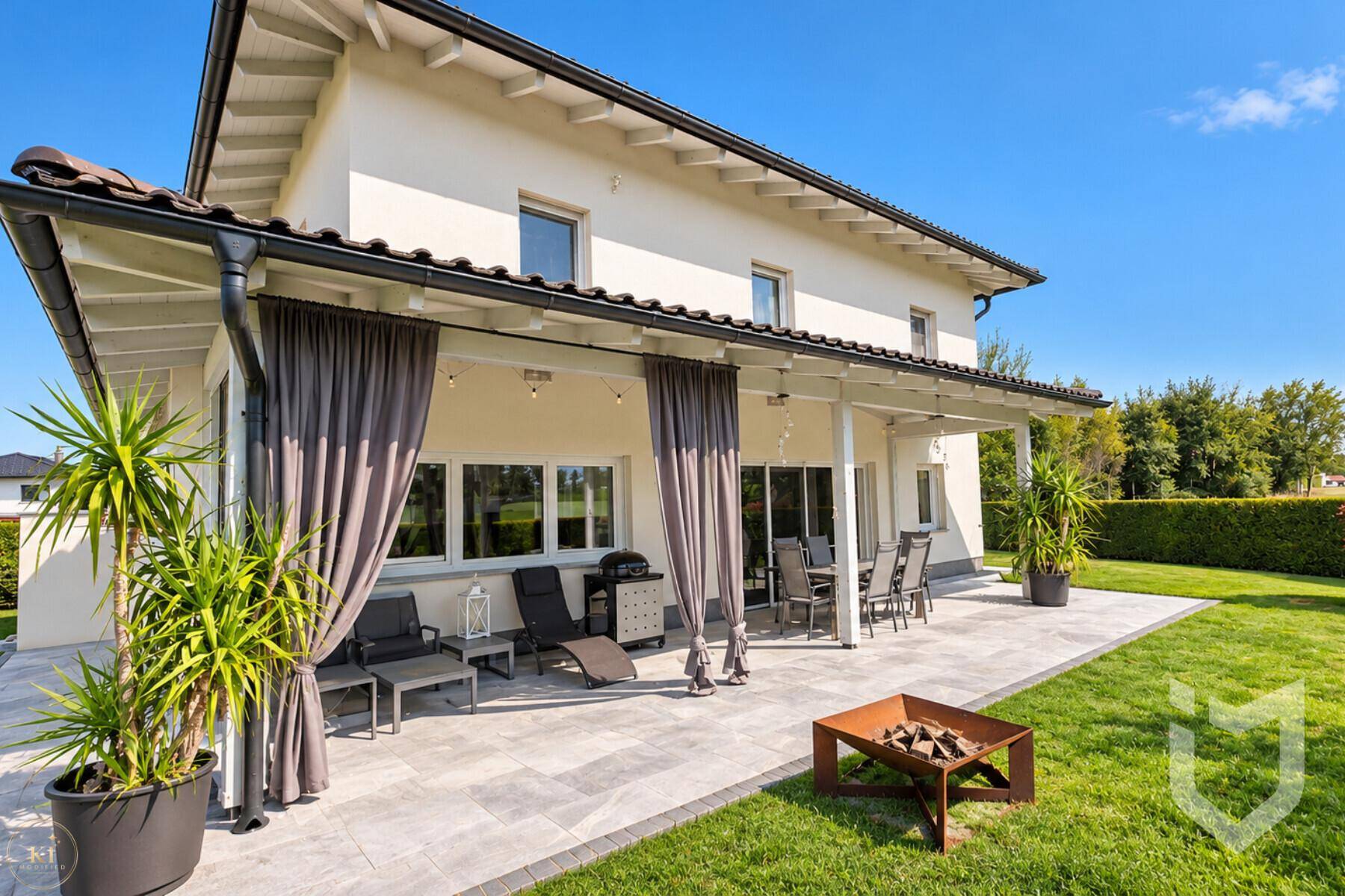 Überdachte Terrasse mit Lounge-Möbeln, Esstisch und Feuerstelle im Gartenbereich.