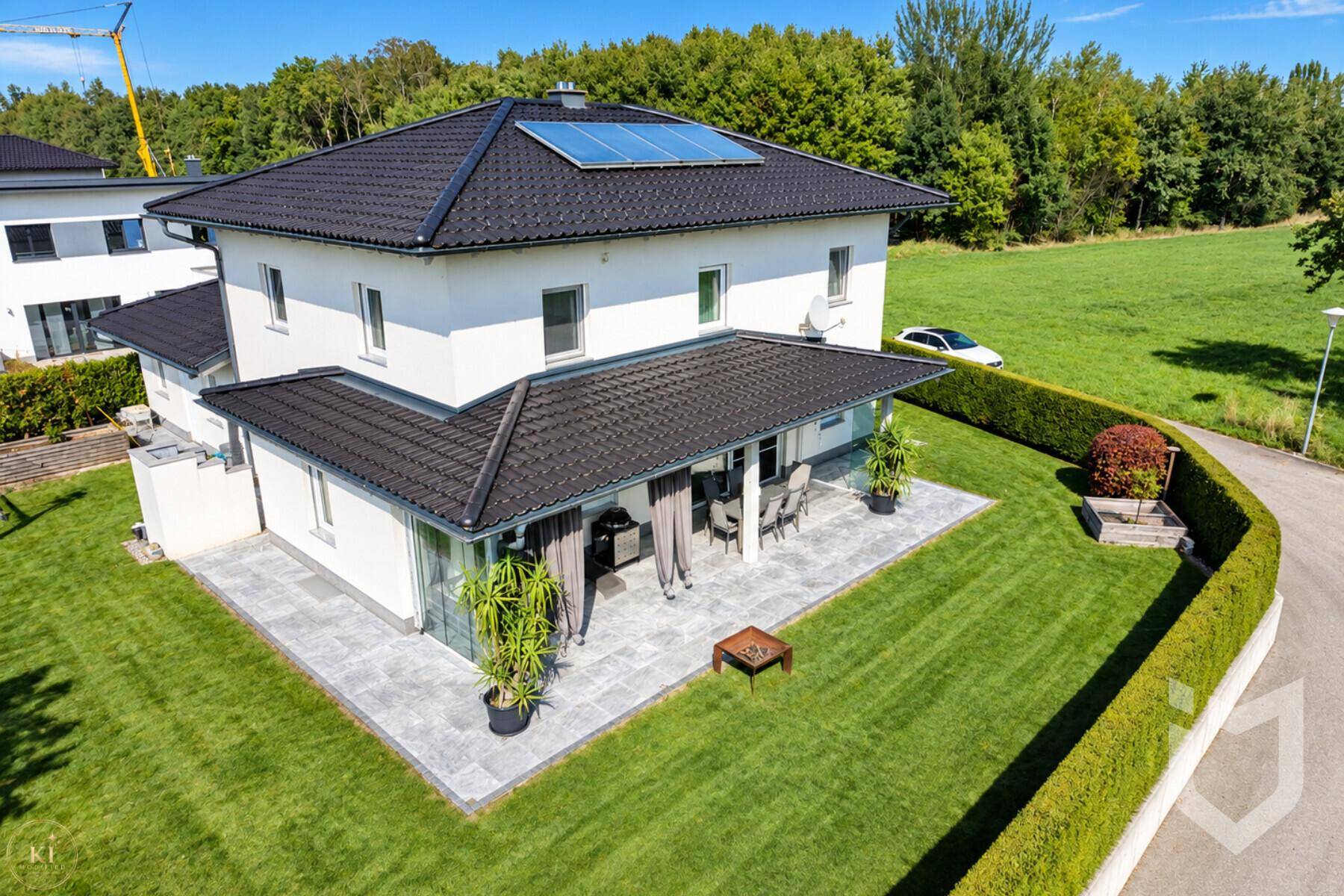 Rückansicht des Hauses mit großer Terrasse, Rasenfläche und angrenzendem Grünland.