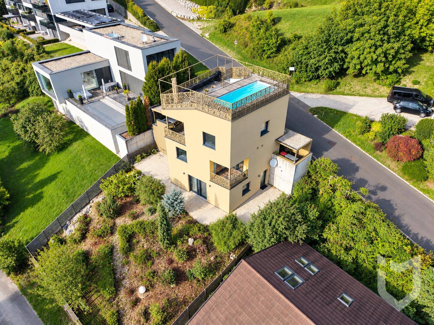 Luftaufnahme des modernen Gebäudes mit Dachpool und angrenzenden Häusern in grüner Umgebung.