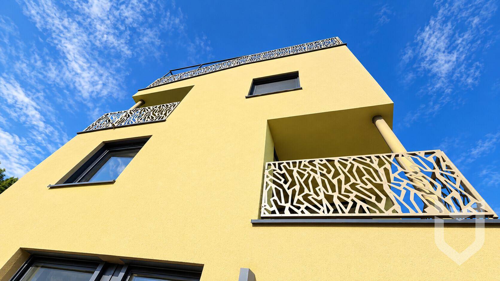Detailansicht der modernen Fassade mit dekorativen Balkongeländern unter blauem Himmel.
