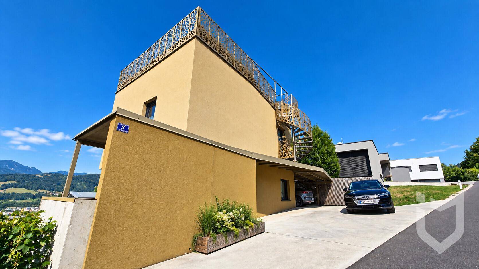 Seitenansicht des modernen Hauses mit Carport und Zufahrt, umgeben von grüner Landschaft.