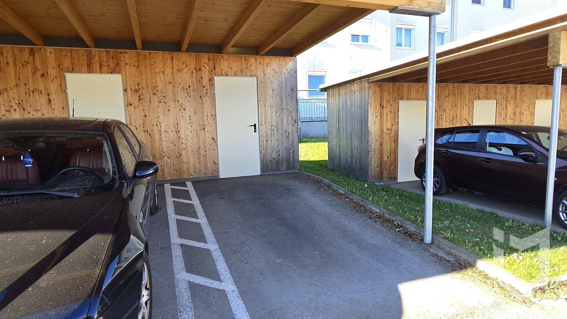 Überdachte Stellplätze in einem Carport-Bereich mit Holzverkleidung und angrenzender Grünfläche.