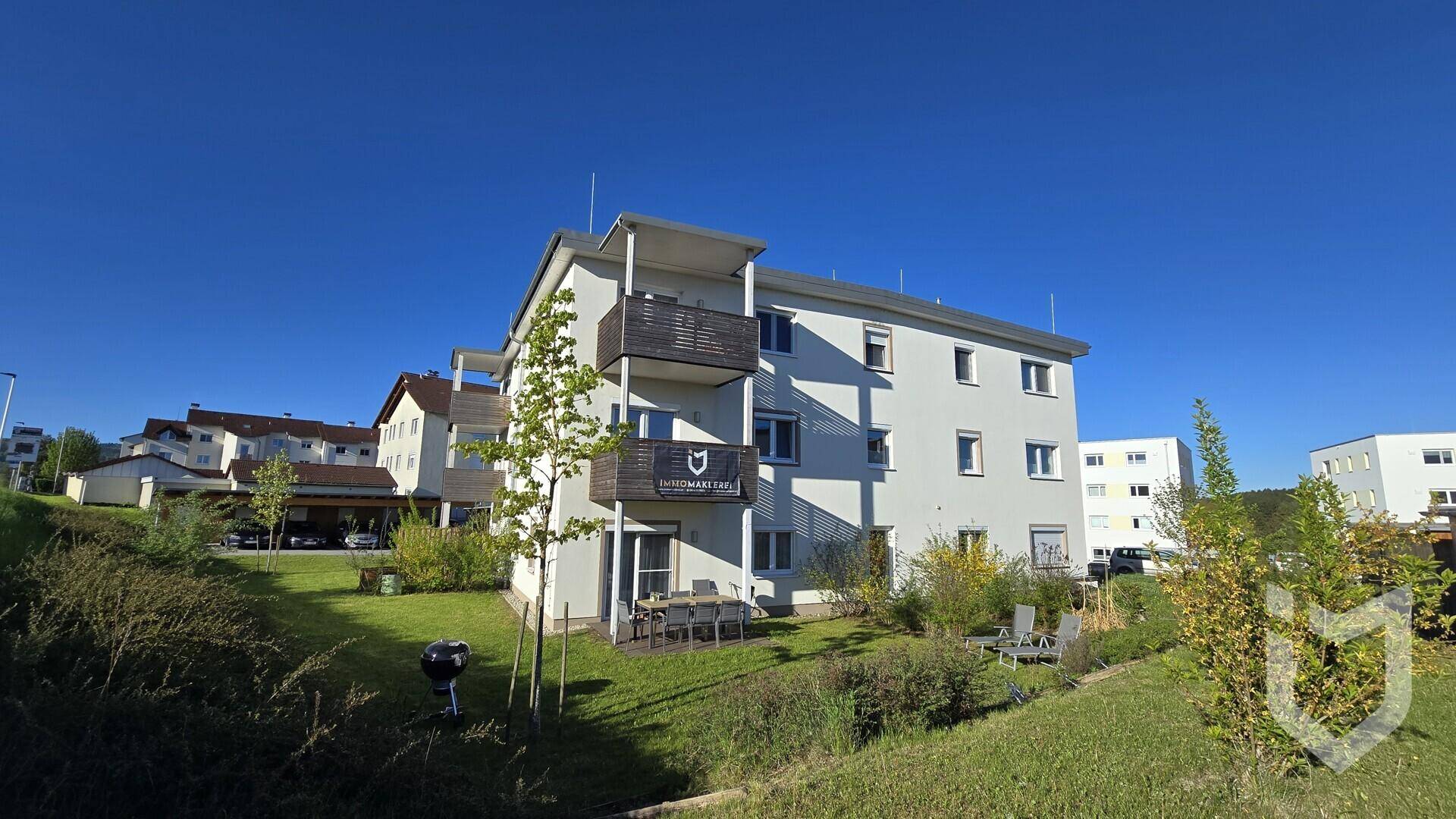 Mehrfamilienhaus mit Balkonen und einer gepflegten Grünfläche im Außenbereich unter blauem Himmel.