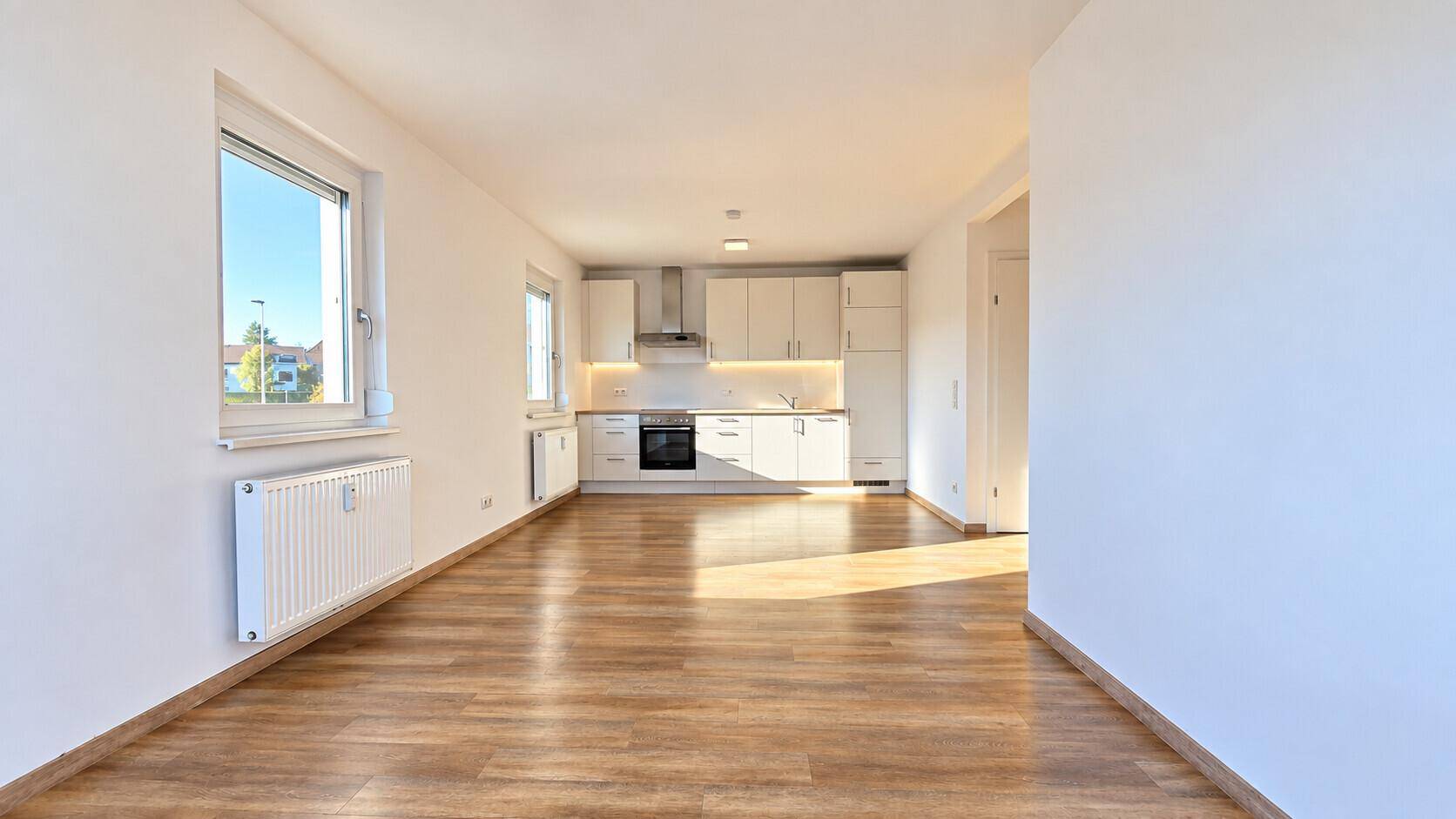 Lichtdurchfluteter offener Wohnbereich mit moderner Einbauküche und hellem Laminatboden.