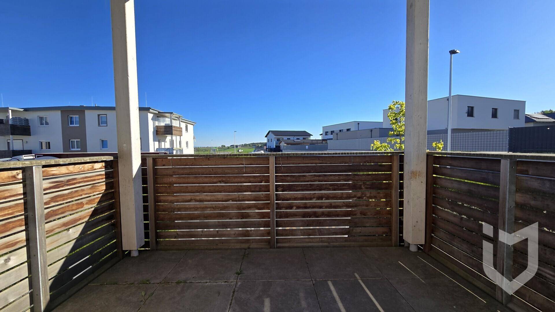 Geräumige Terrasse mit Holzzaun und Blick auf die umliegende Bebauung unter klarem Himmel.