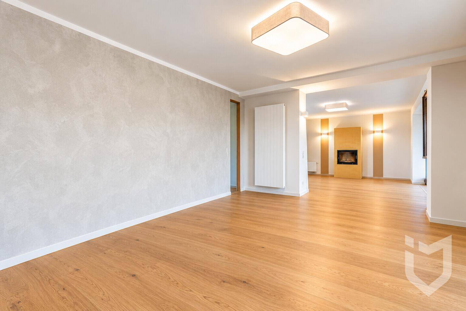 Geräumiges, unmöbliertes Wohnzimmer mit hellem Parkettboden und einem Kamin im Hintergrund.