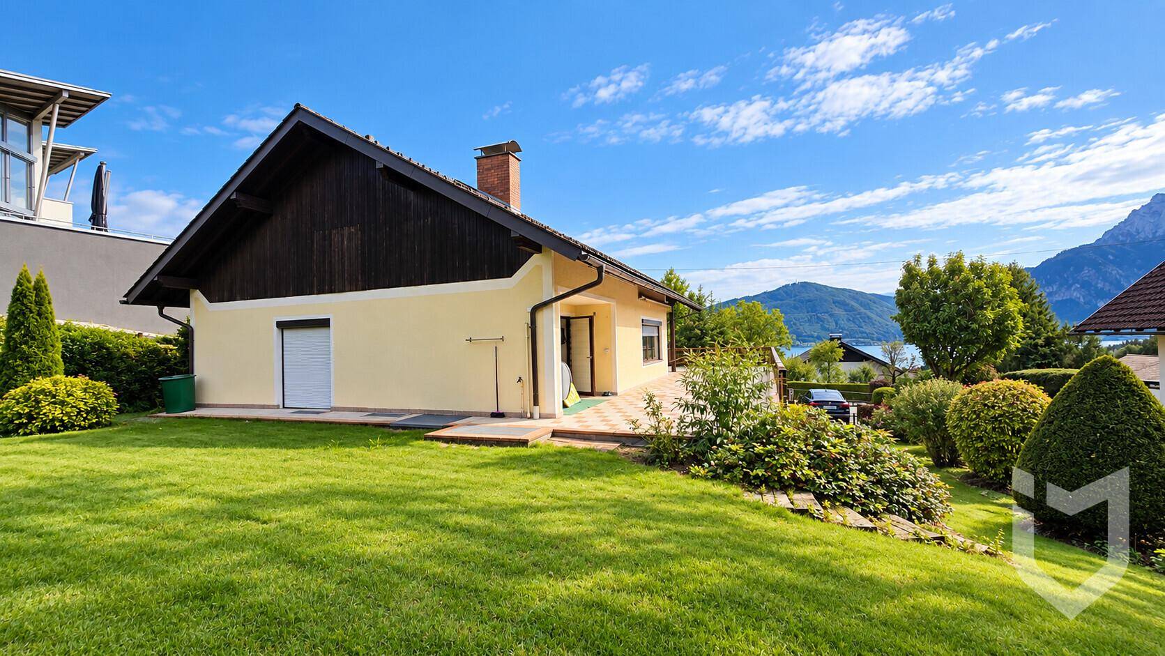 Rückseite des Hauses mit großem Rasenbereich, Terrasse und Blick auf den See und die Berge.
