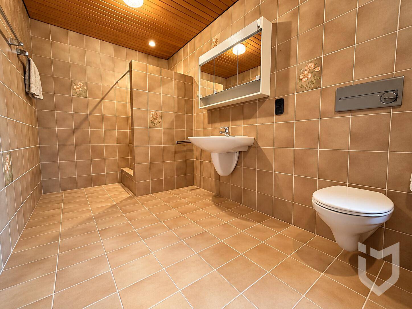 Badezimmer mit braunen Fliesen, Holzdecke, wandhängendem WC und ebenerdiger Dusche.