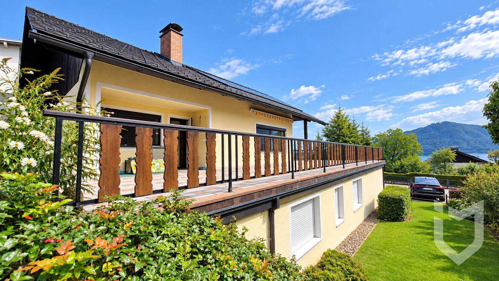 Seitenansicht des Hauses mit langem Balkon, Blick auf den See und die umliegende Landschaft.