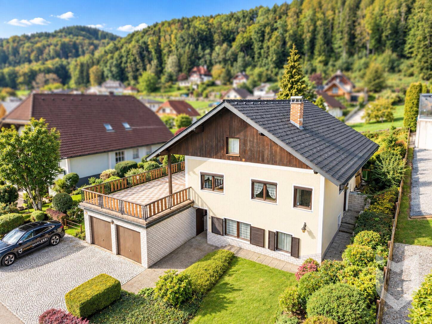 Luftaufnahme eines Einfamilienhauses mit Terrasse über der Doppelgarage und gepflegtem Garten.