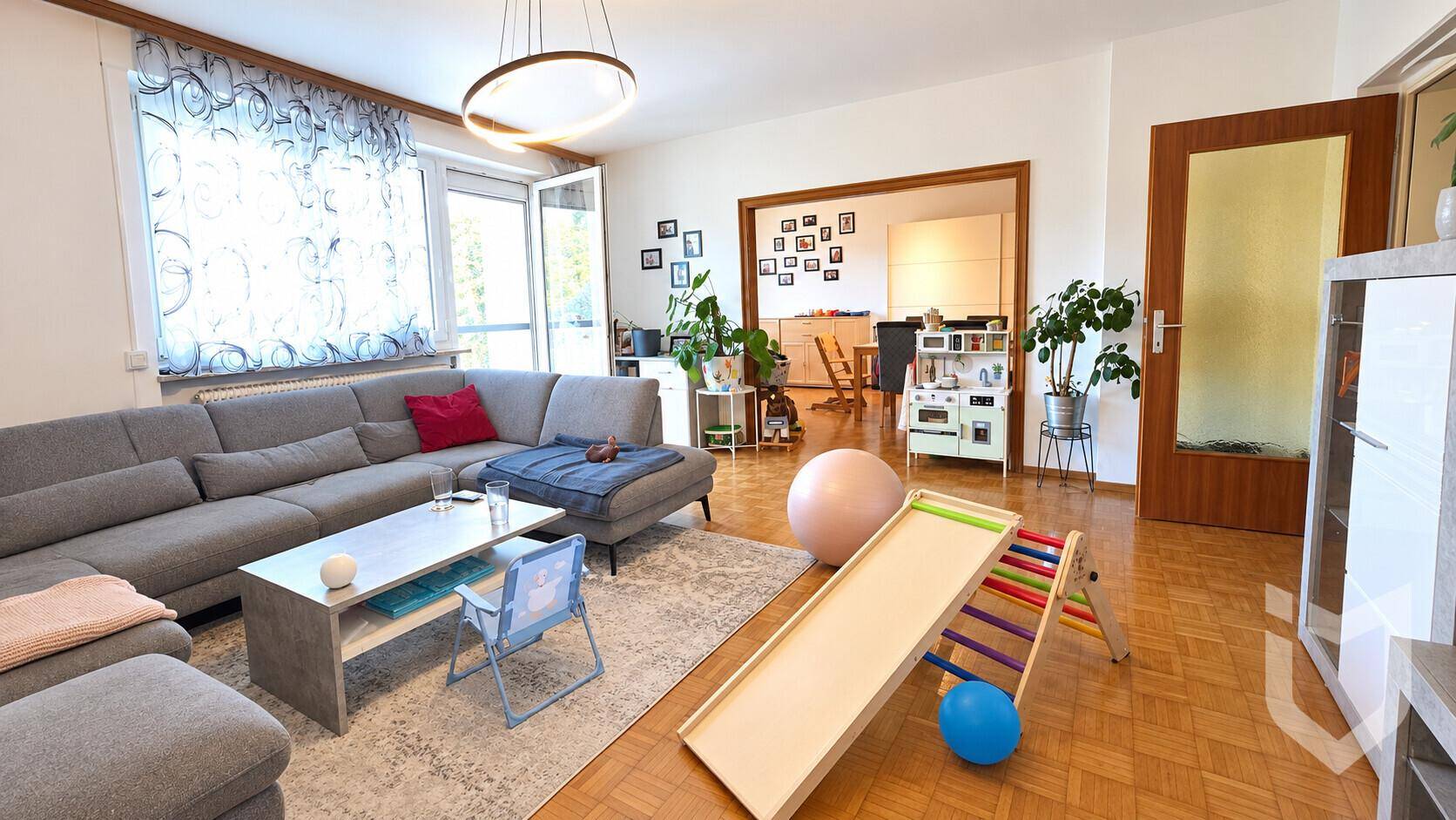 Geräumiges Wohnzimmer mit großem Ecksofa, Parkettboden und Zugang zum Essbereich.