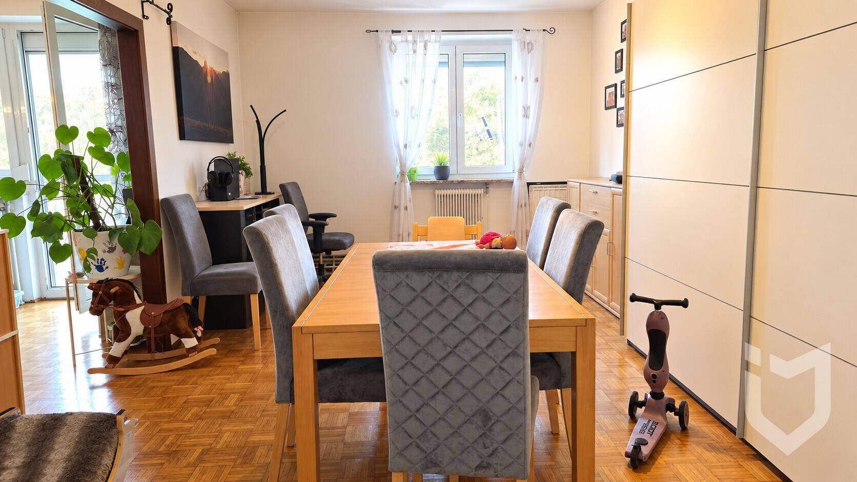 Esszimmer mit Holztisch, gepolsterten Stühlen und Parkettboden, hell durch großes Fenster.
