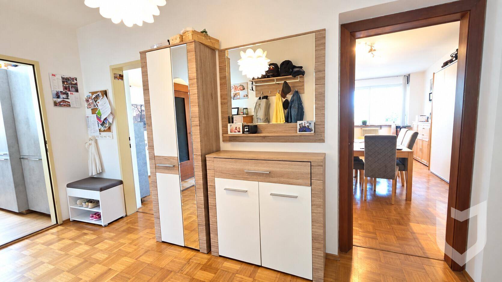 Eingangsbereich mit Holzparkett, Garderobe und Spiegel, der den Blick in den Essbereich freigibt.