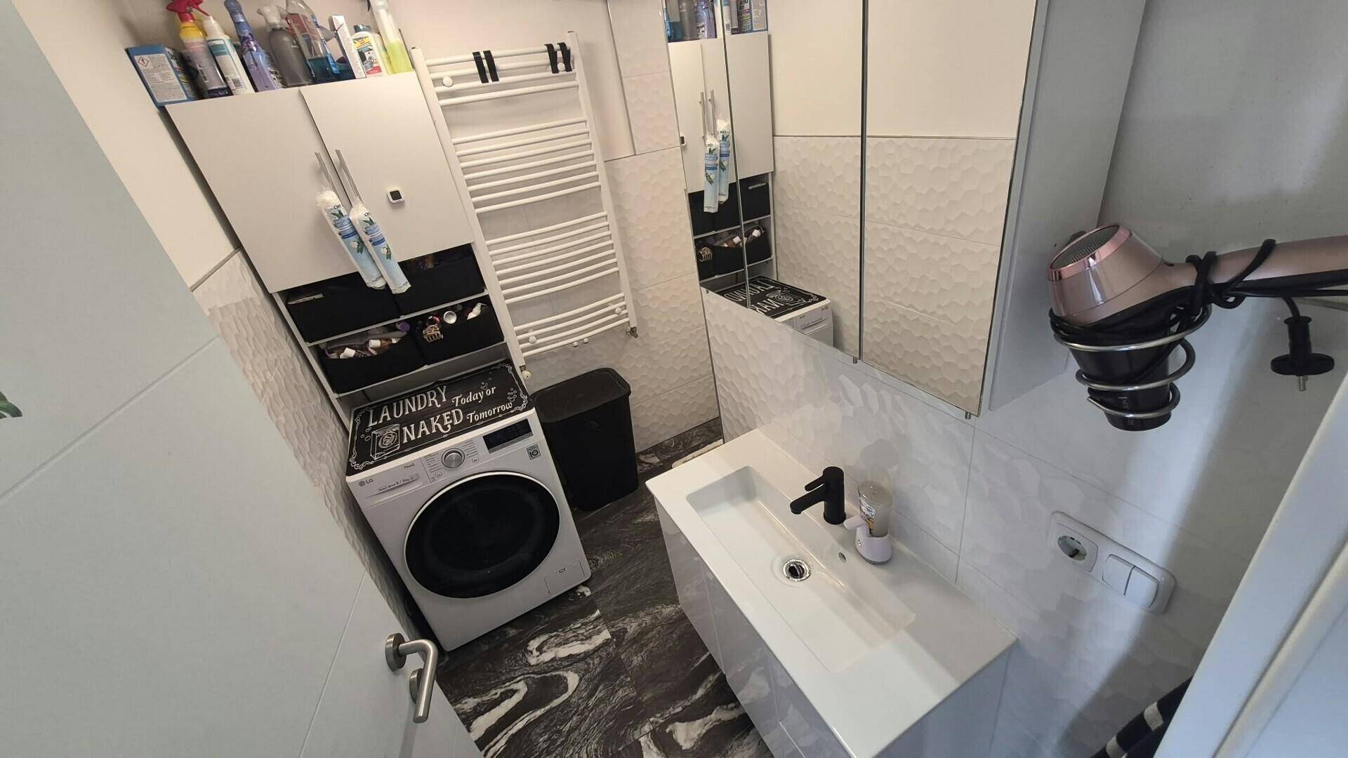 Modernes Badezimmer mit Waschbecken, beheiztem Handtuchhalter und Spiegelschrank.