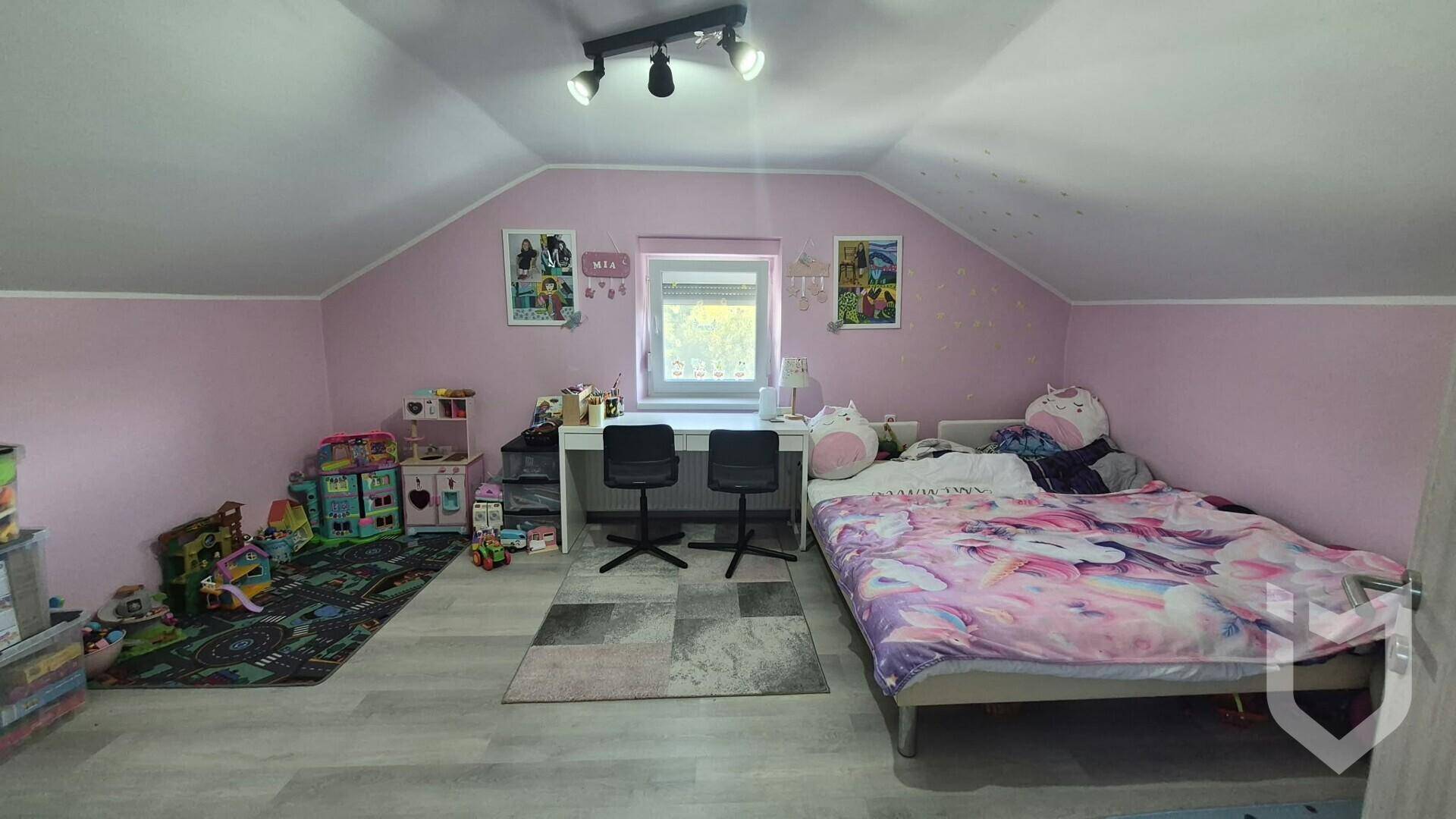 Kinderzimmer mit rosa Wänden, Bett, Schreibtisch und Spielzeug unter der Dachschräge.