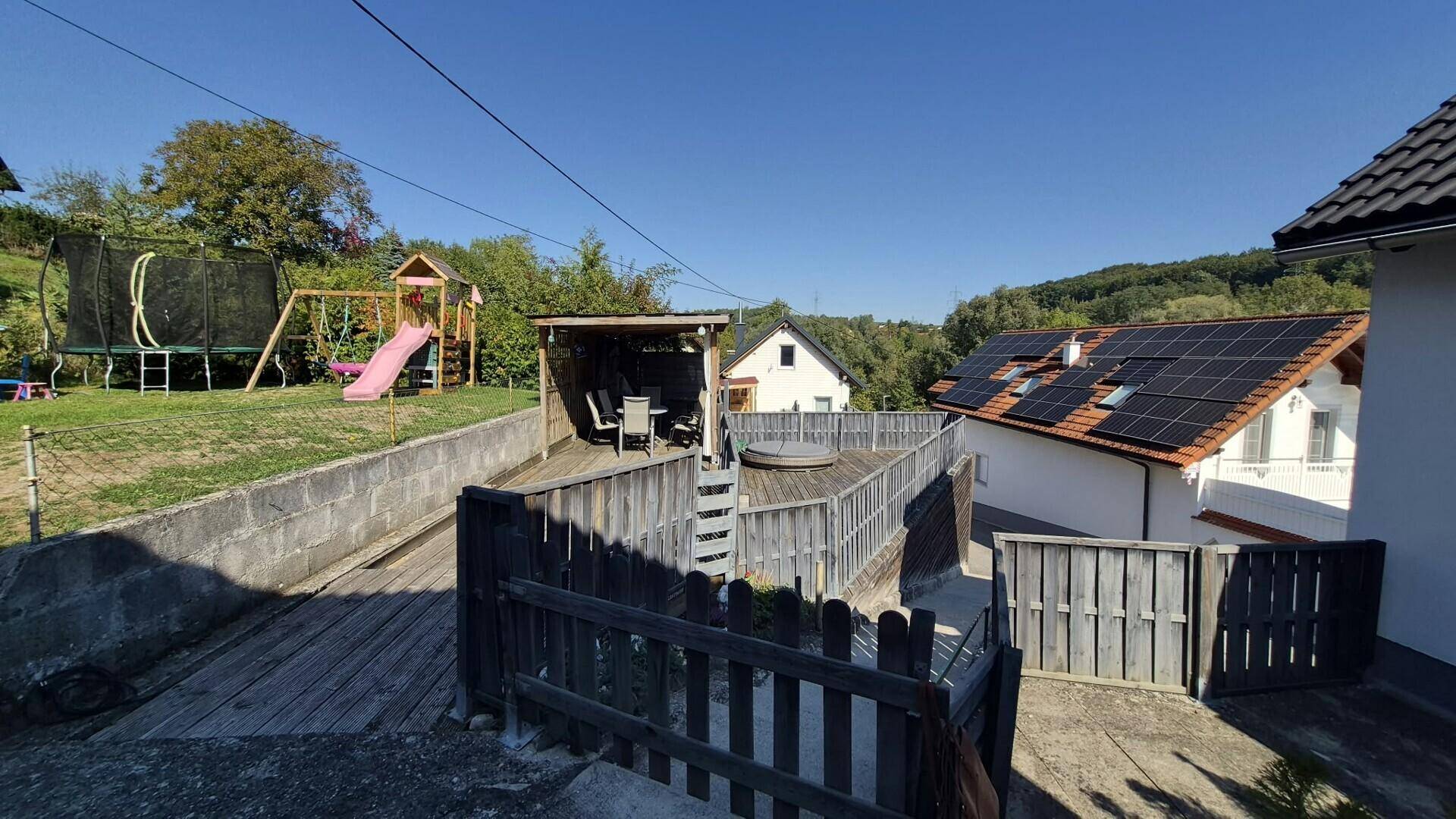 Weitläufiger Gartenbereich mit Trampolin, Spielplatz, überdachtem Sitzplatz und Holzterrasse.