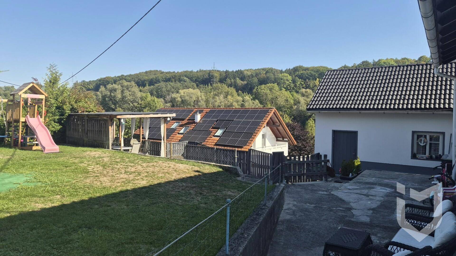 Großer Garten mit Spielplatz, überdachtem Sitzbereich und Photovoltaikanlage auf dem Dach.