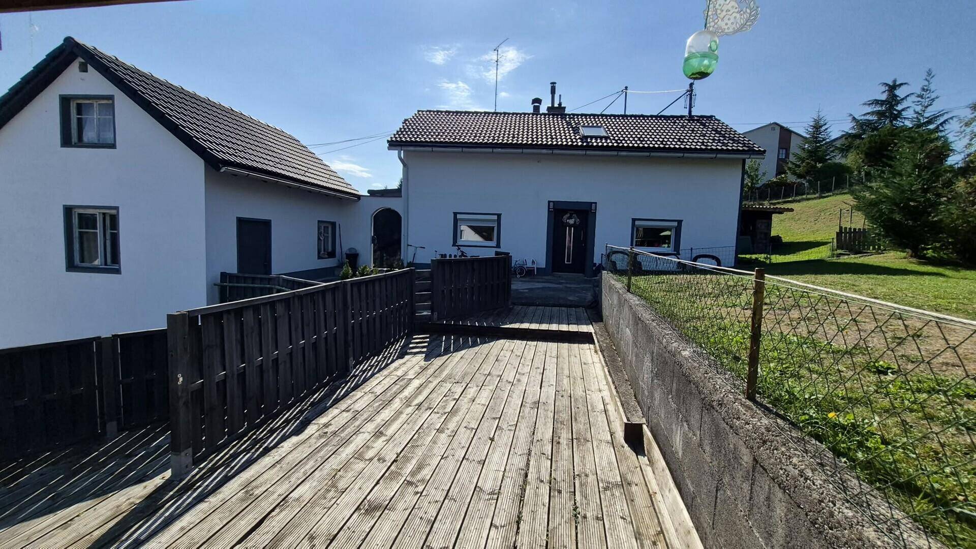 Weitläufige Holzterrasse mit Blick auf das Haus und die grüne Umgebung unter blauem Himmel.