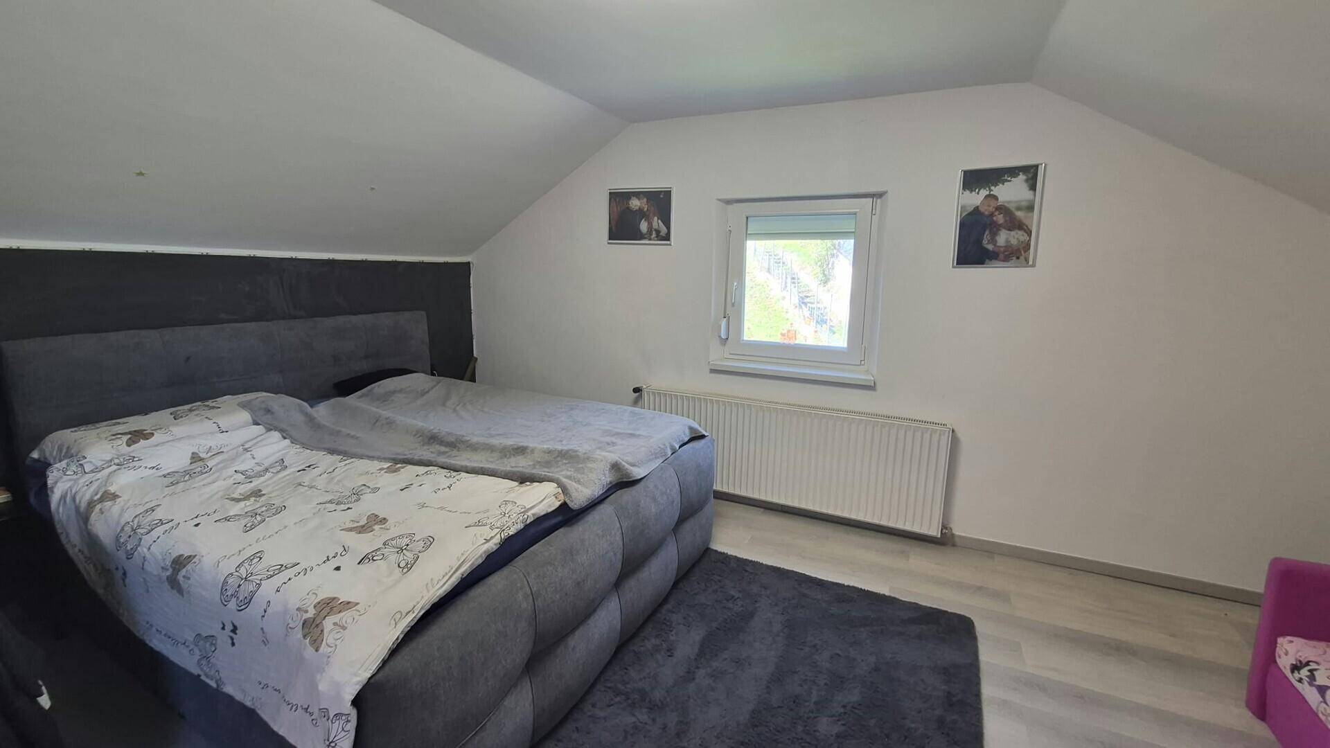 Gemütliches Schlafzimmer mit großem Bett, Dachschräge und Fenster für natürliches Licht.