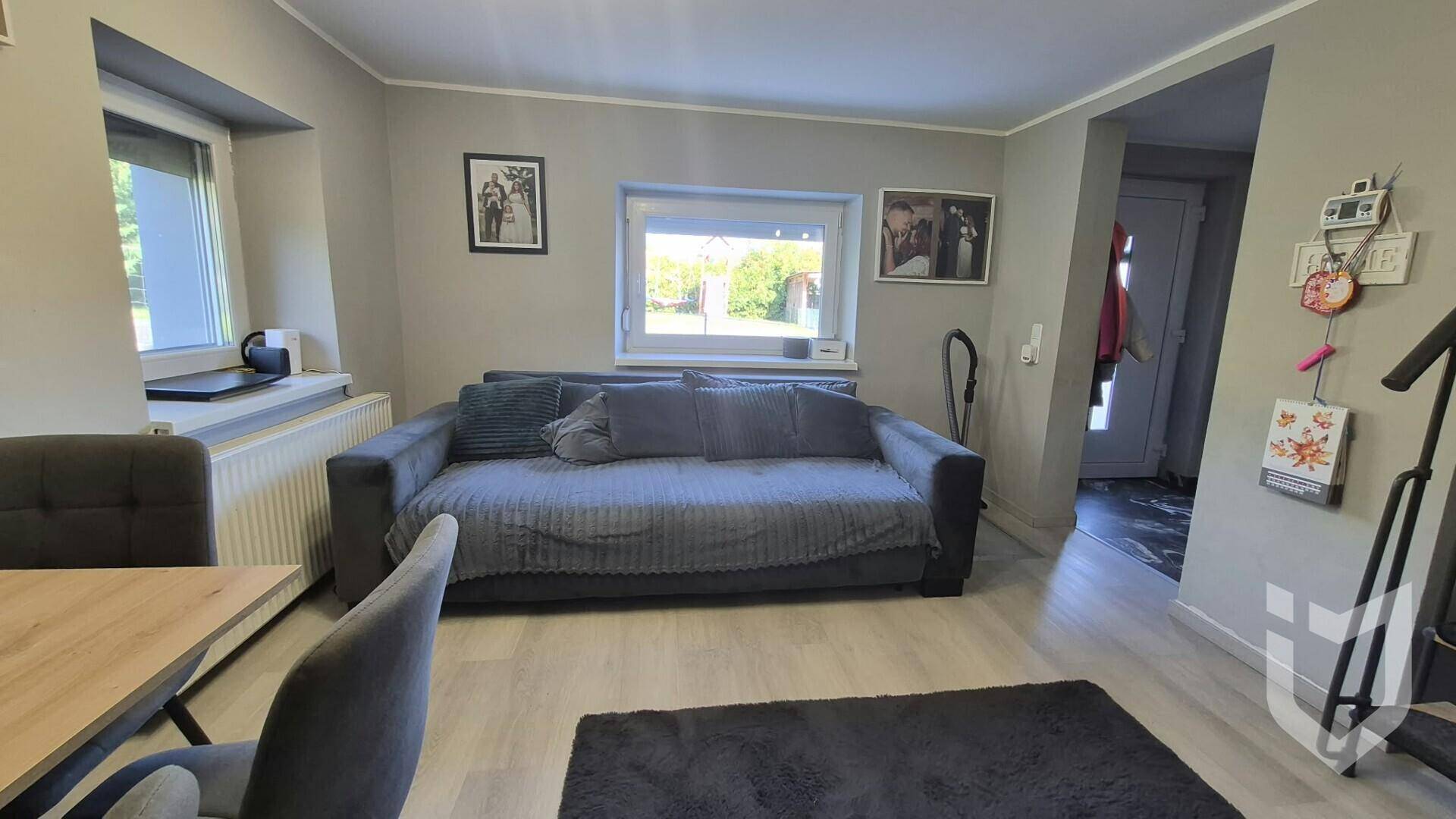 Heller Wohnbereich mit bequemem grauen Sofa, Heizkörper und Fenstern für natürliches Licht.
