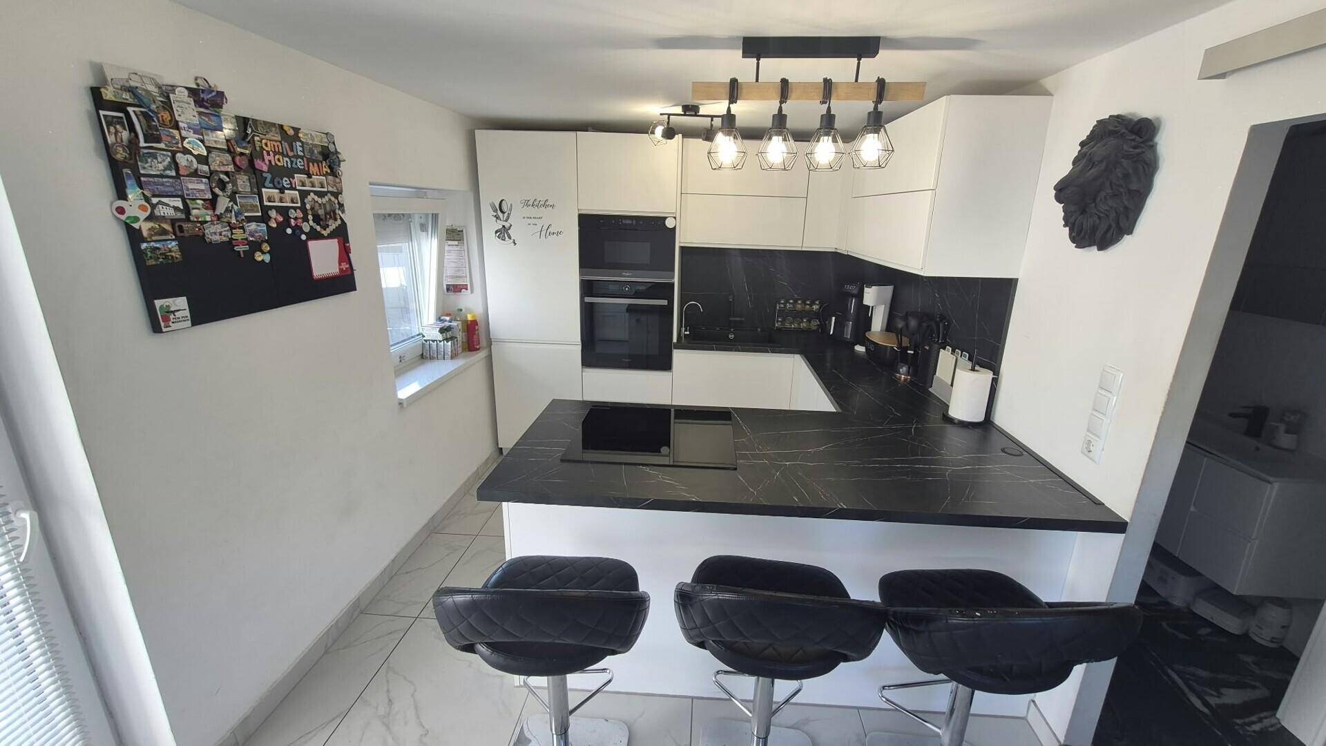 Moderne Küche mit weißen Schränken, dunkler Arbeitsplatte und einer Frühstücksbar mit Hockern.