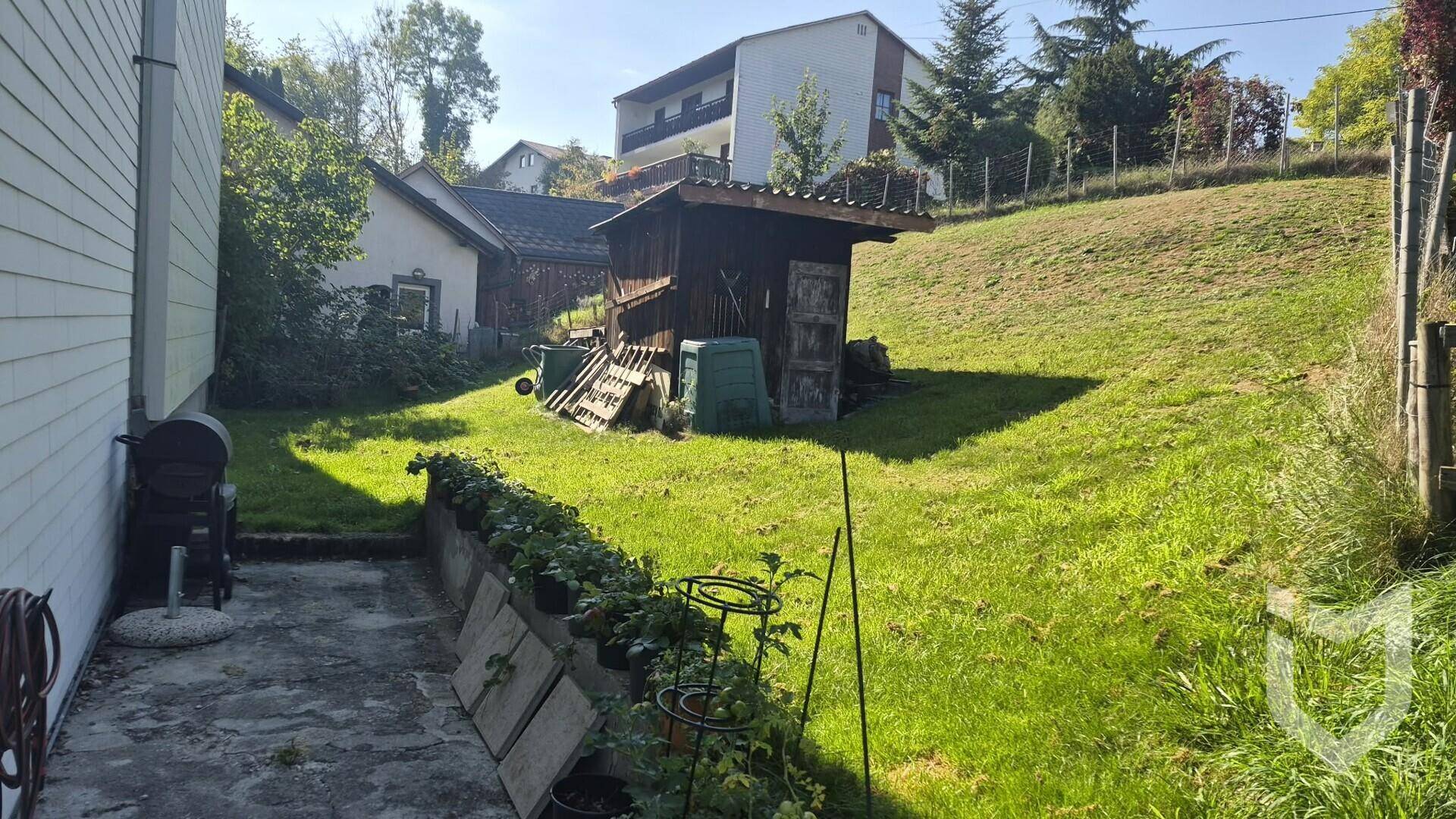 Hanglage-Garten mit Rasenfläche, Gartenhaus und bepflanzten Beeten in sonniger Umgebung.