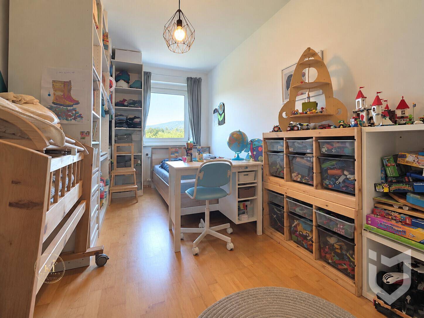 Kinderzimmer mit Bett, Schreibtisch und Spielzeugregalen, hell und funktional eingerichtet.