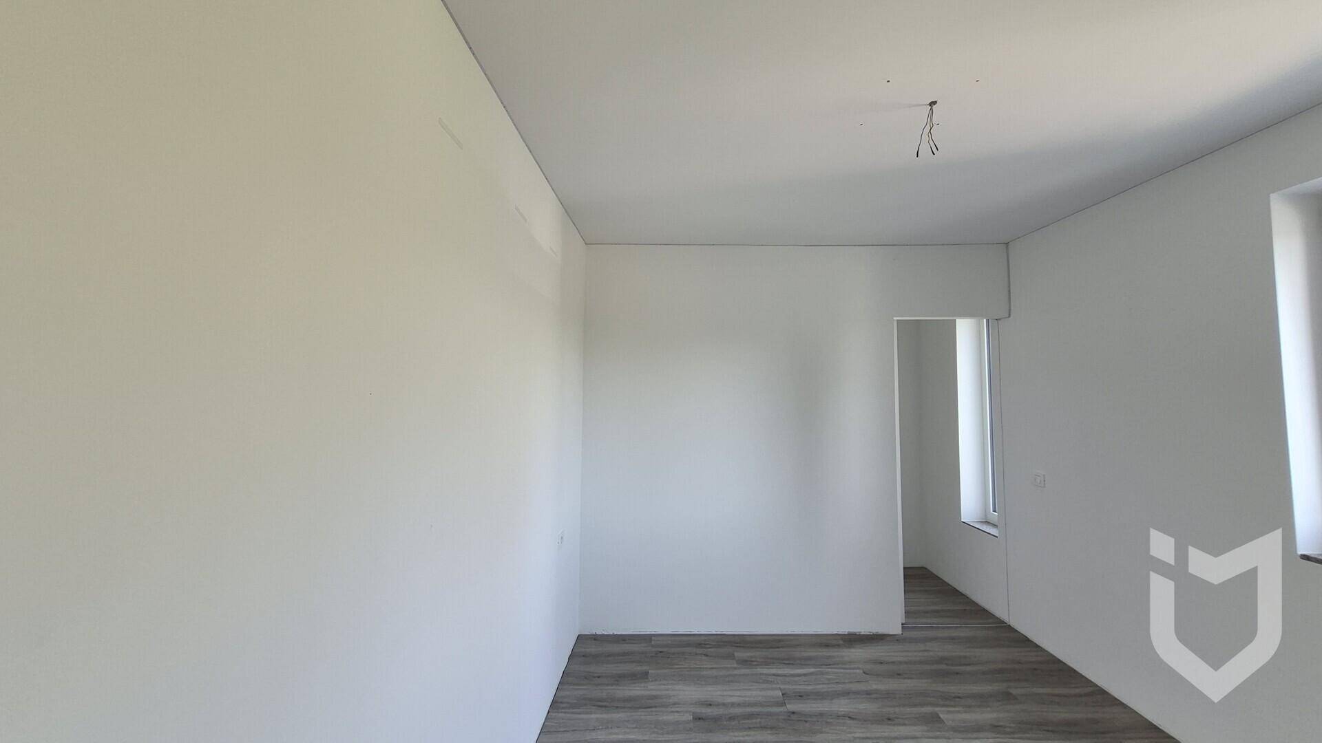 Leerer Raum mit Laminatboden und weiß gestrichenen Wänden.