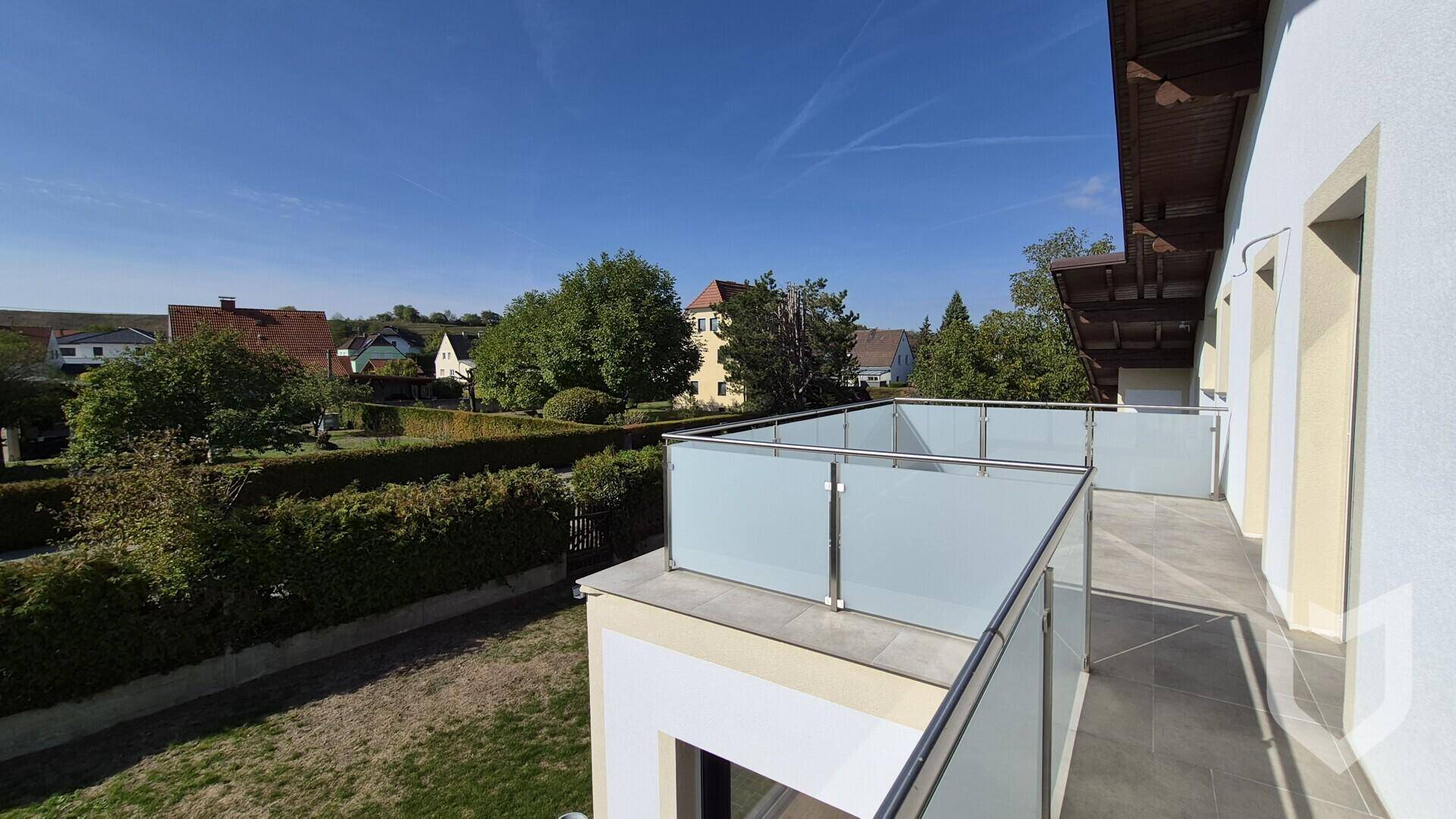 Großer Balkon mit Glasgeländer und Blick auf die grüne Umgebung.