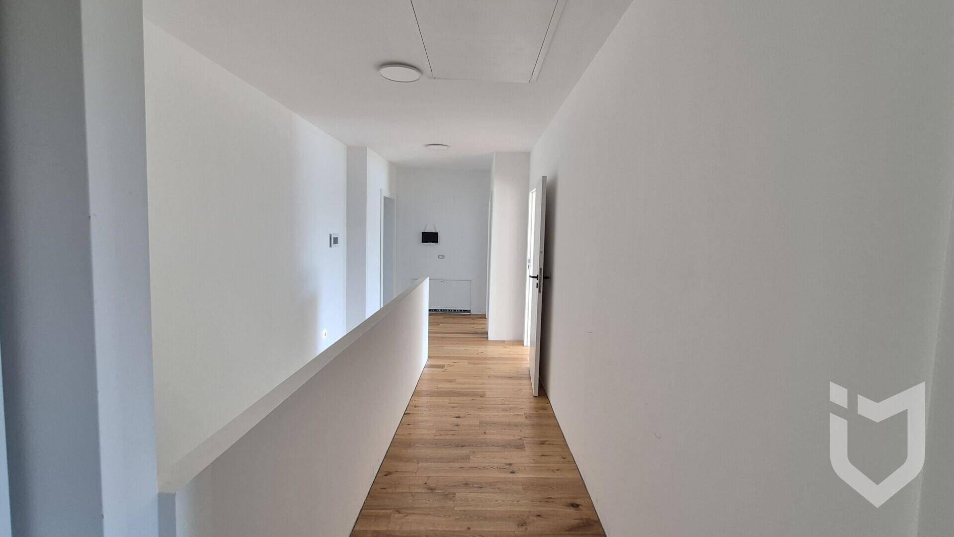Heller Flur im Obergeschoss mit Holzboden und weiß gestrichenen Wänden.