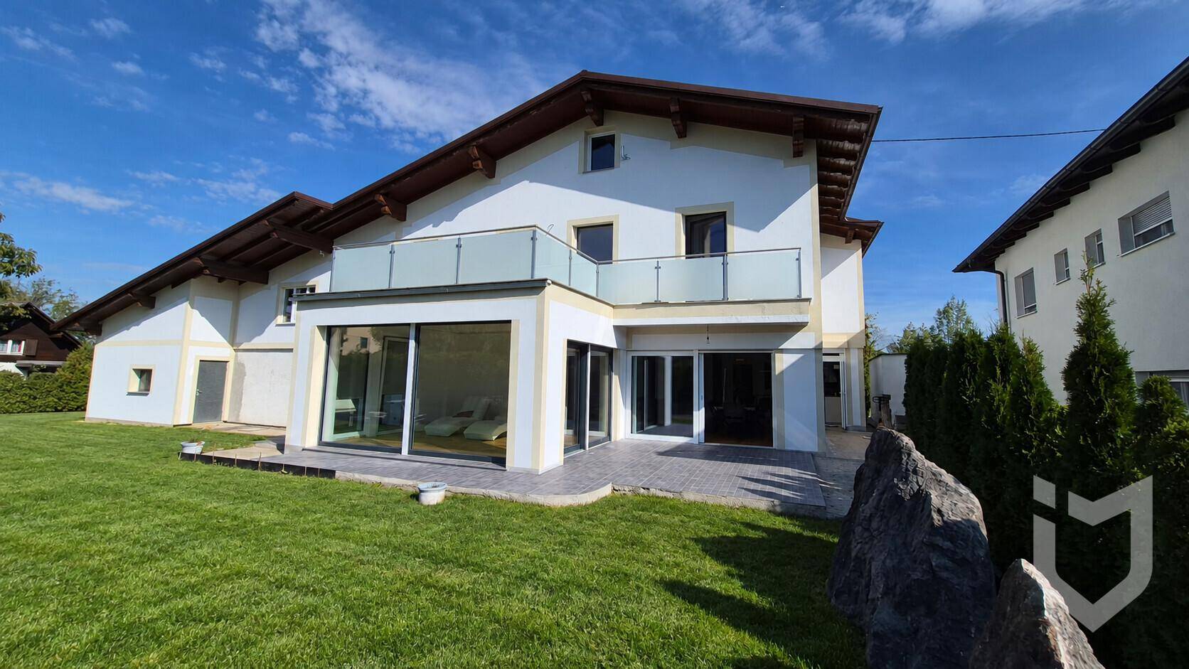 Moderne Hausfassade mit großen Glasfronten, Balkon und gepflegtem Rasen.