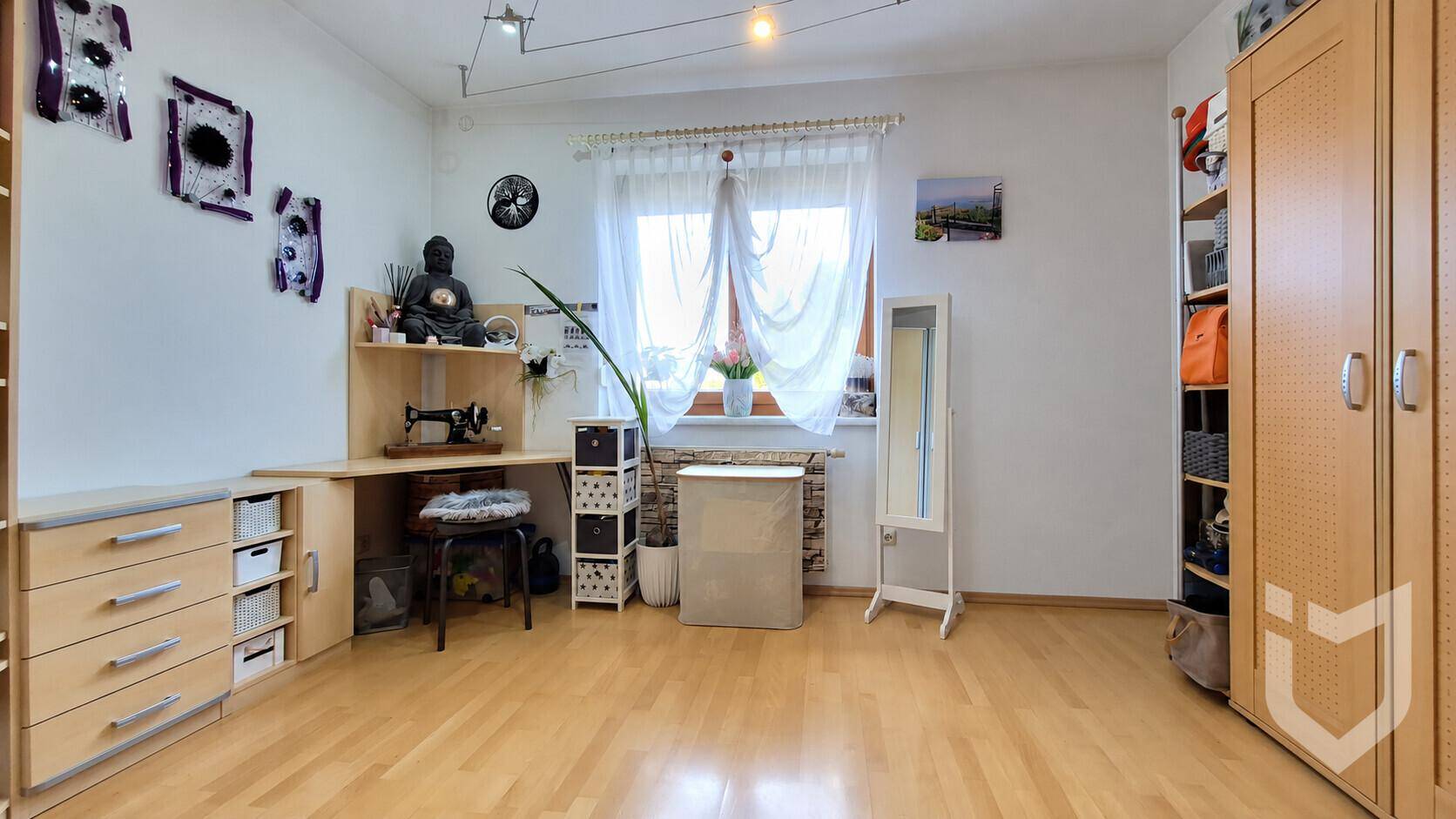 Helles Arbeitszimmer mit Holzfußboden, Schreibtisch und Regalen, gut beleuchtet durch ein Fenster.