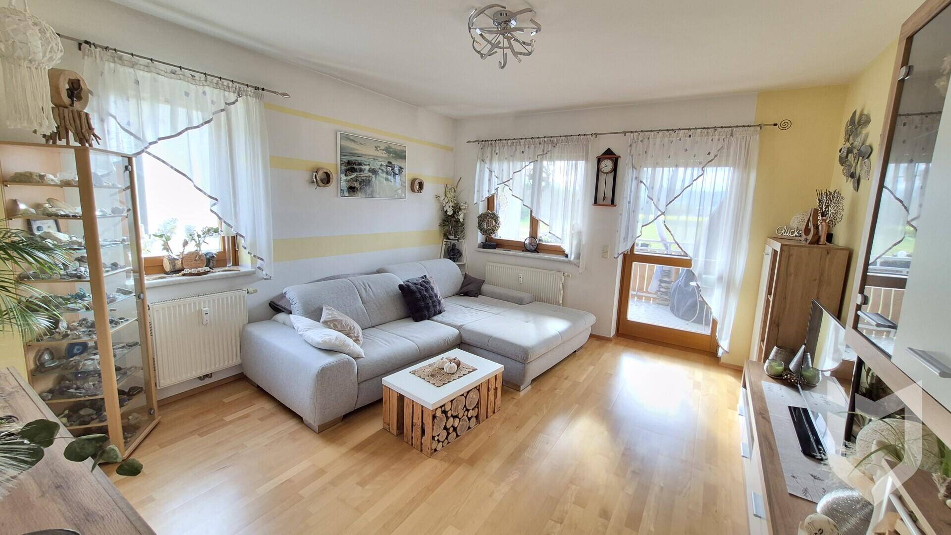 Geräumiges Wohnzimmer mit beigem Ecksofa, Holzfußboden und Zugang zu einem Balkon.