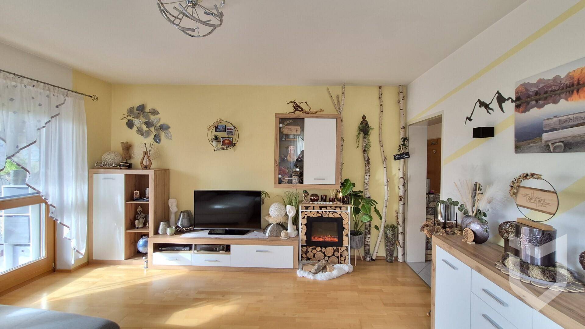 Wohnzimmer mit Sofa, Fernseher und einem dekorativen Kamin, umgeben von Holzdekoration.