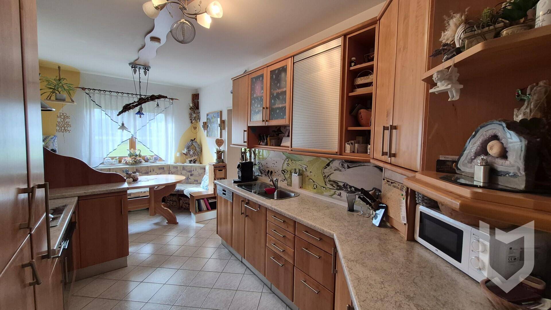 Geräumige Küche mit Holzfronten, Arbeitsplatten und einem Essbereich im Hintergrund.