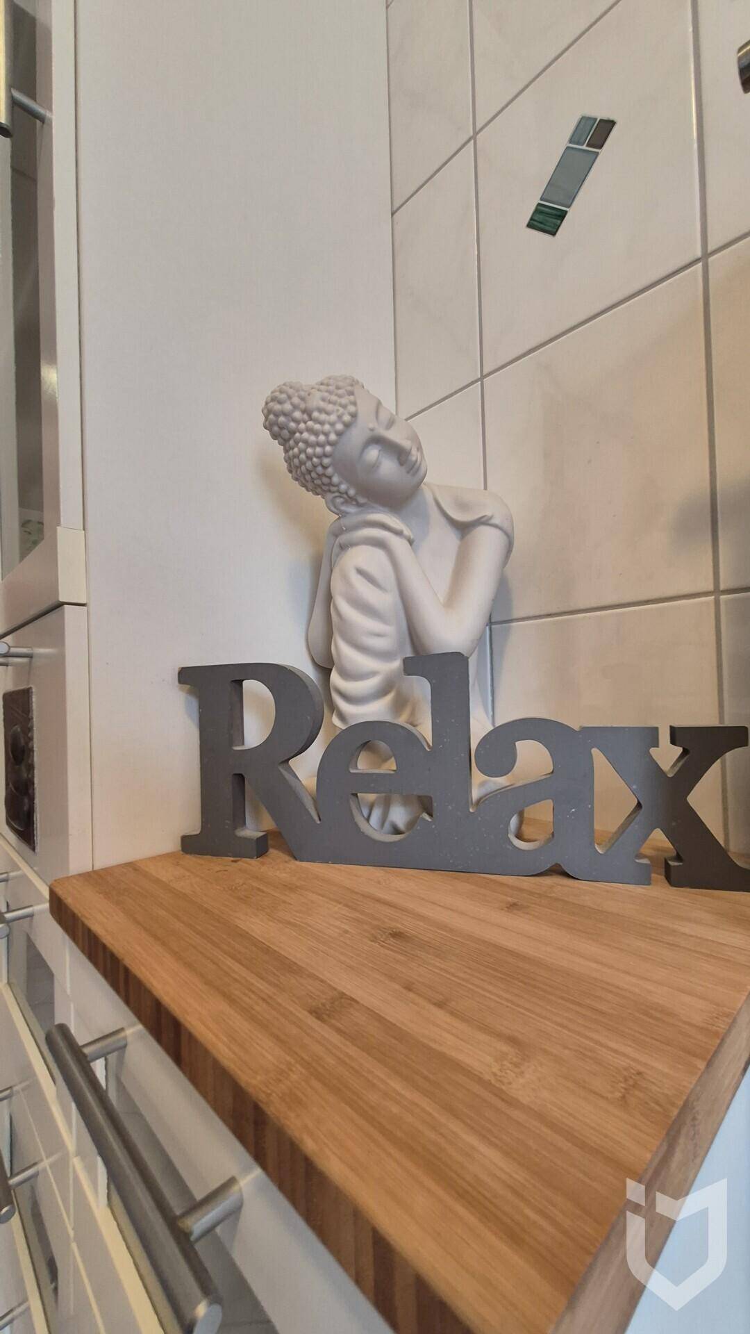 Detailaufnahme einer Buddha-Statue und eines 'Relax'-Schriftzugs auf einer Holzablage.