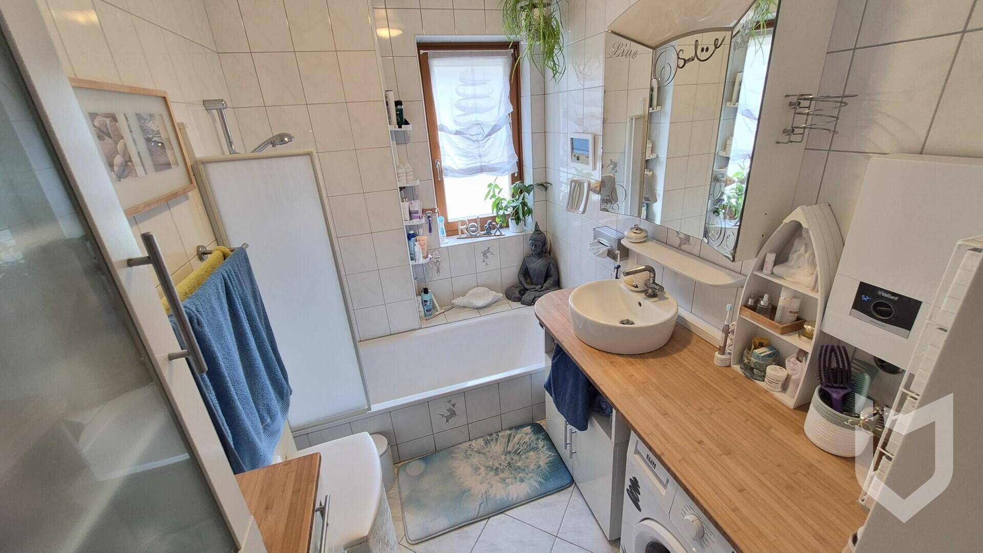 Gefliestes Badezimmer mit Badewanne, Waschbecken auf Holzplatte und einem Fenster.