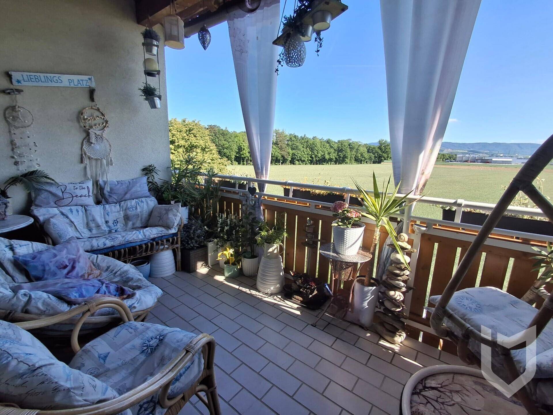 Gemütliche Loggia mit Sitzgelegenheiten und weitem Blick über grüne Felder und die Landschaft.