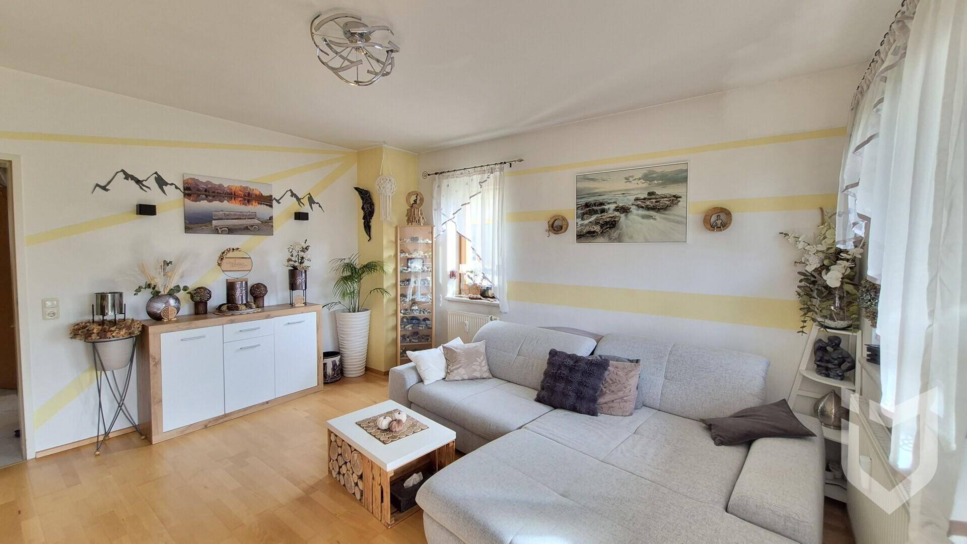 Helles Wohnzimmer mit Ecksofa, Holzfußboden und dekorativen Wandstreifen in Gelb.