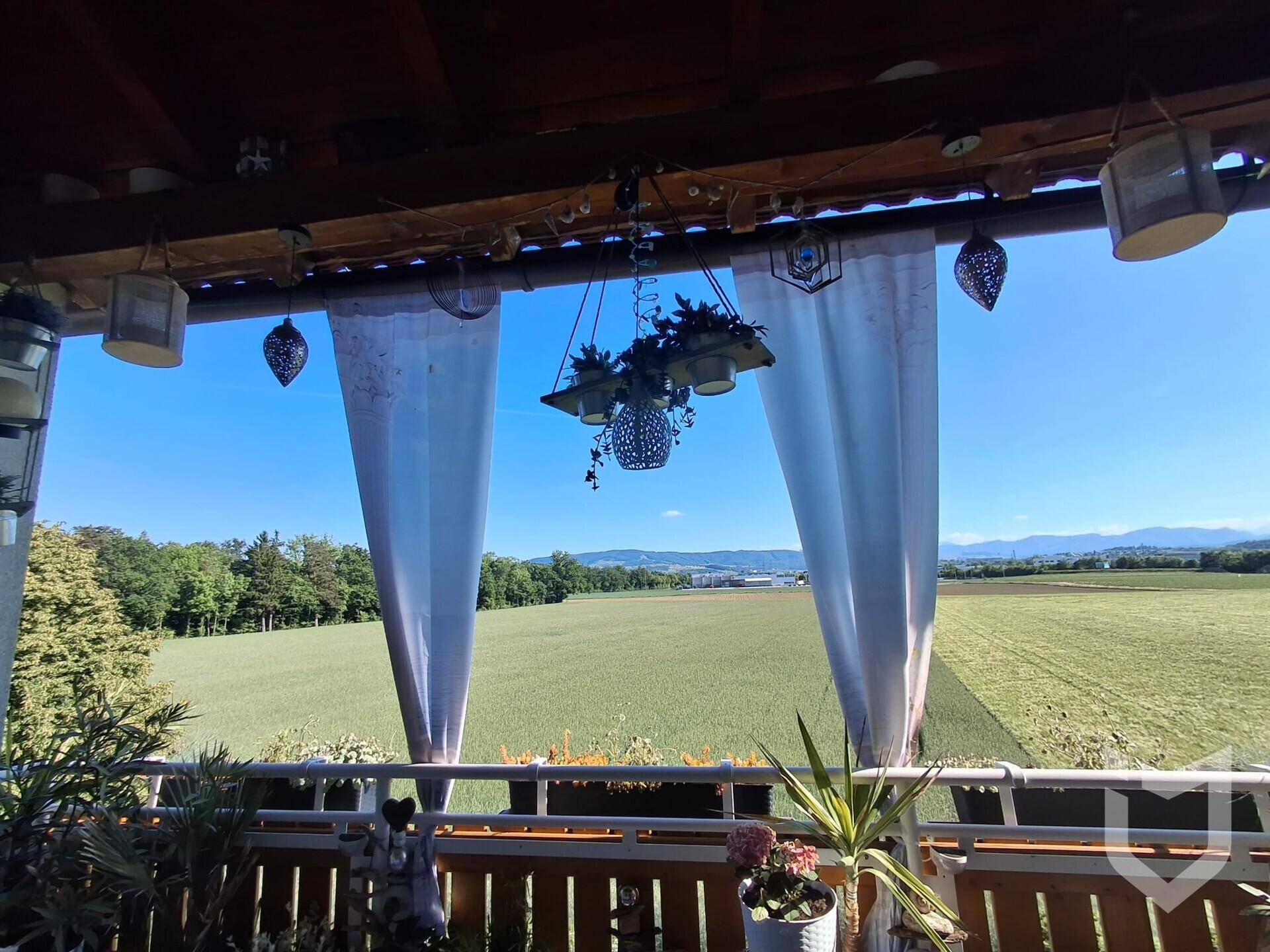 Helle Loggia mit Vorhängen und weitem Ausblick auf grüne Felder und die umliegende Natur.