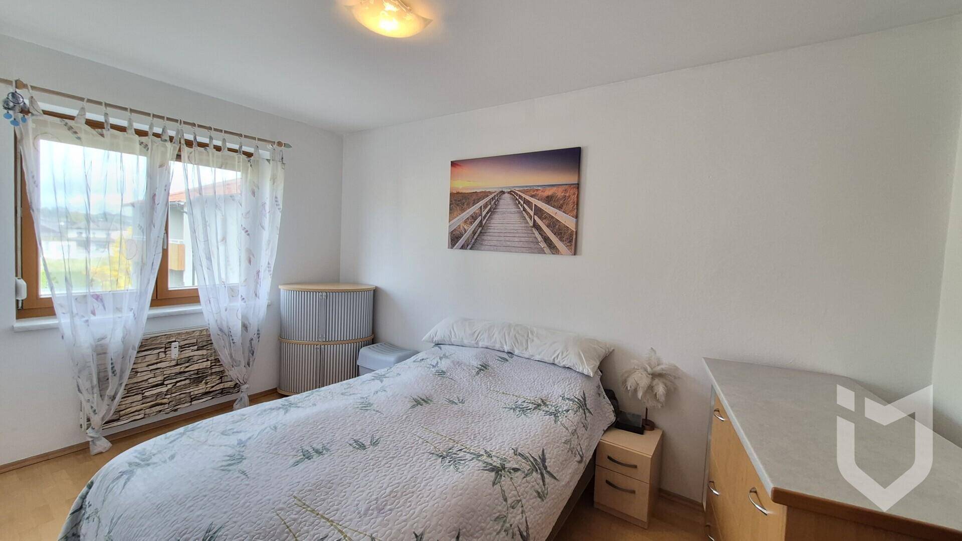 Schlafzimmer mit Einzelbett, Holzfußboden und einem Fenster mit Vorhängen.
